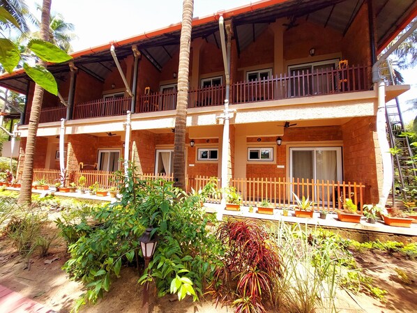 A two-story building with a balcony on each floor, surrounded by potted plants and a wooden fence. - OmBodhi Retreat (Kumta)