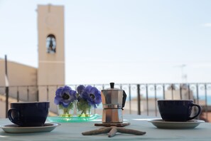 Una mesa con dos tazas, una cafetera, una estrella de mar y un jarrón de flores, con una torre al fondo.