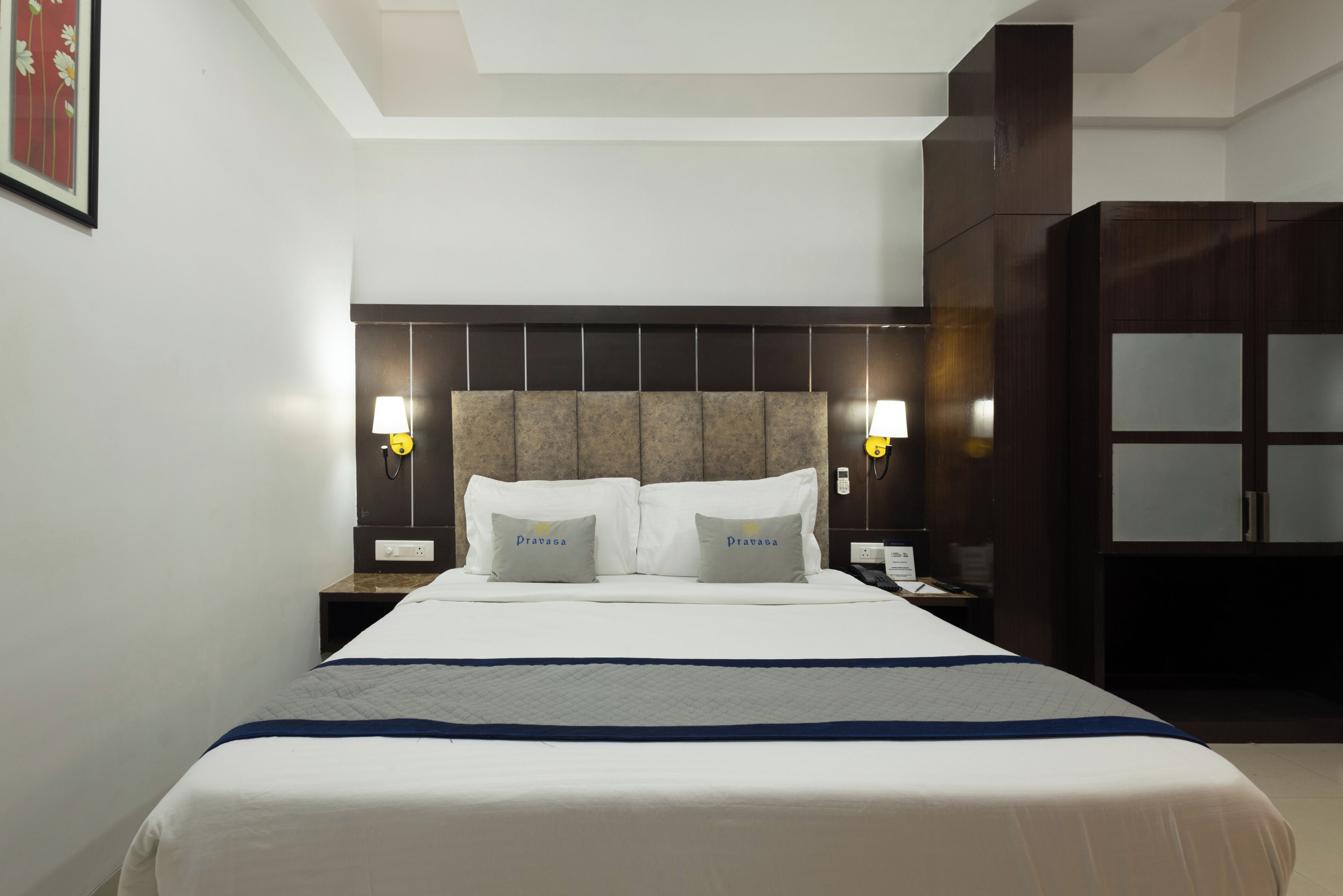 A hotel room with a large bed, two bedside lamps, a headboard, and a wardrobe.
