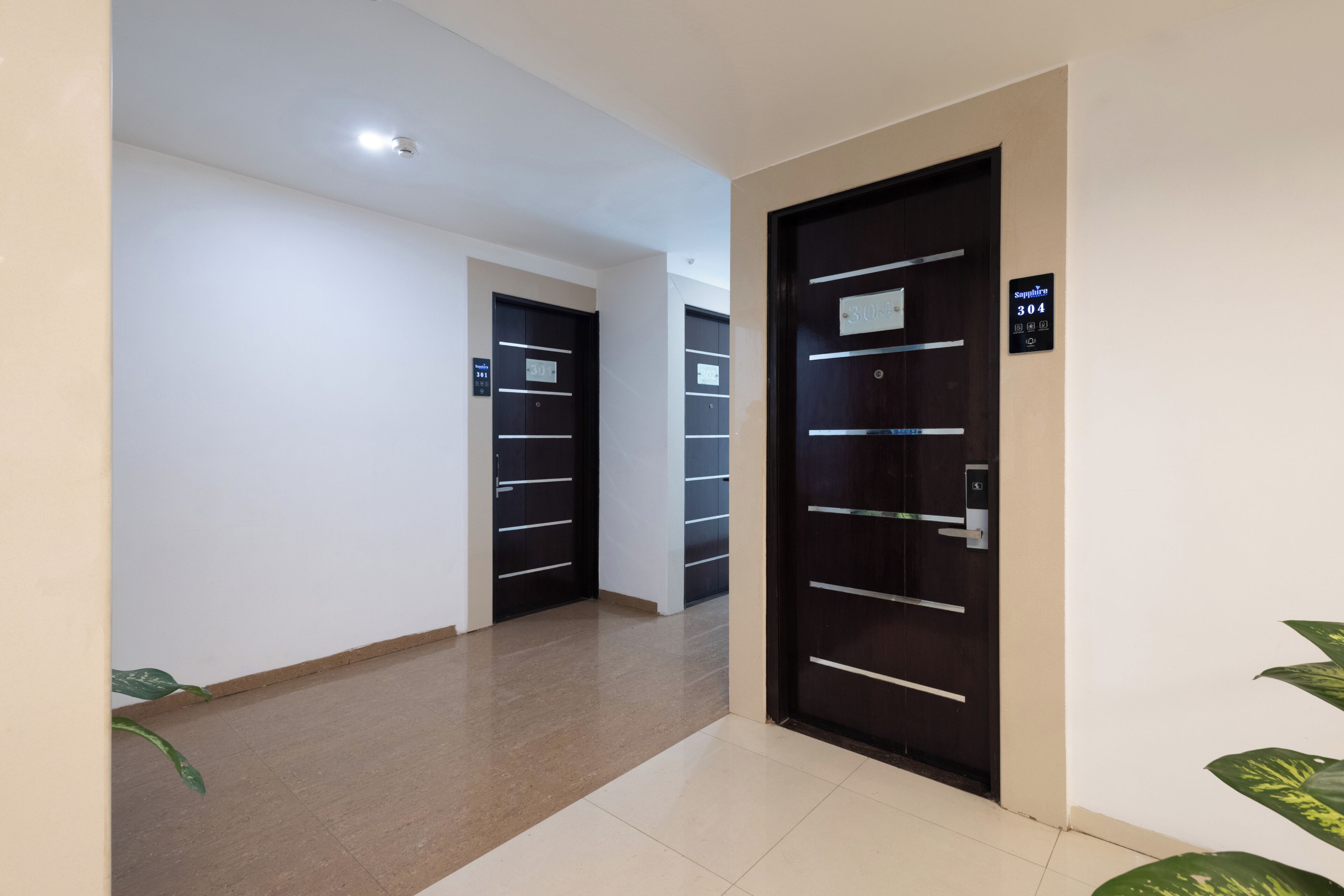 Un corredor de hotel moderno con un diseño limpio y minimalista, que presenta una combinación de puertas de madera oscura y clara, suelo de baldosas y una paleta de colores neutros.