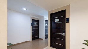 A modern hotel corridor with a clean, minimalist design, featuring a combination of dark and light wood doors, a tiled floor, and a neutral color palette. - Pravasa Hotel by Sapphire, Vadodara (Vadodara)