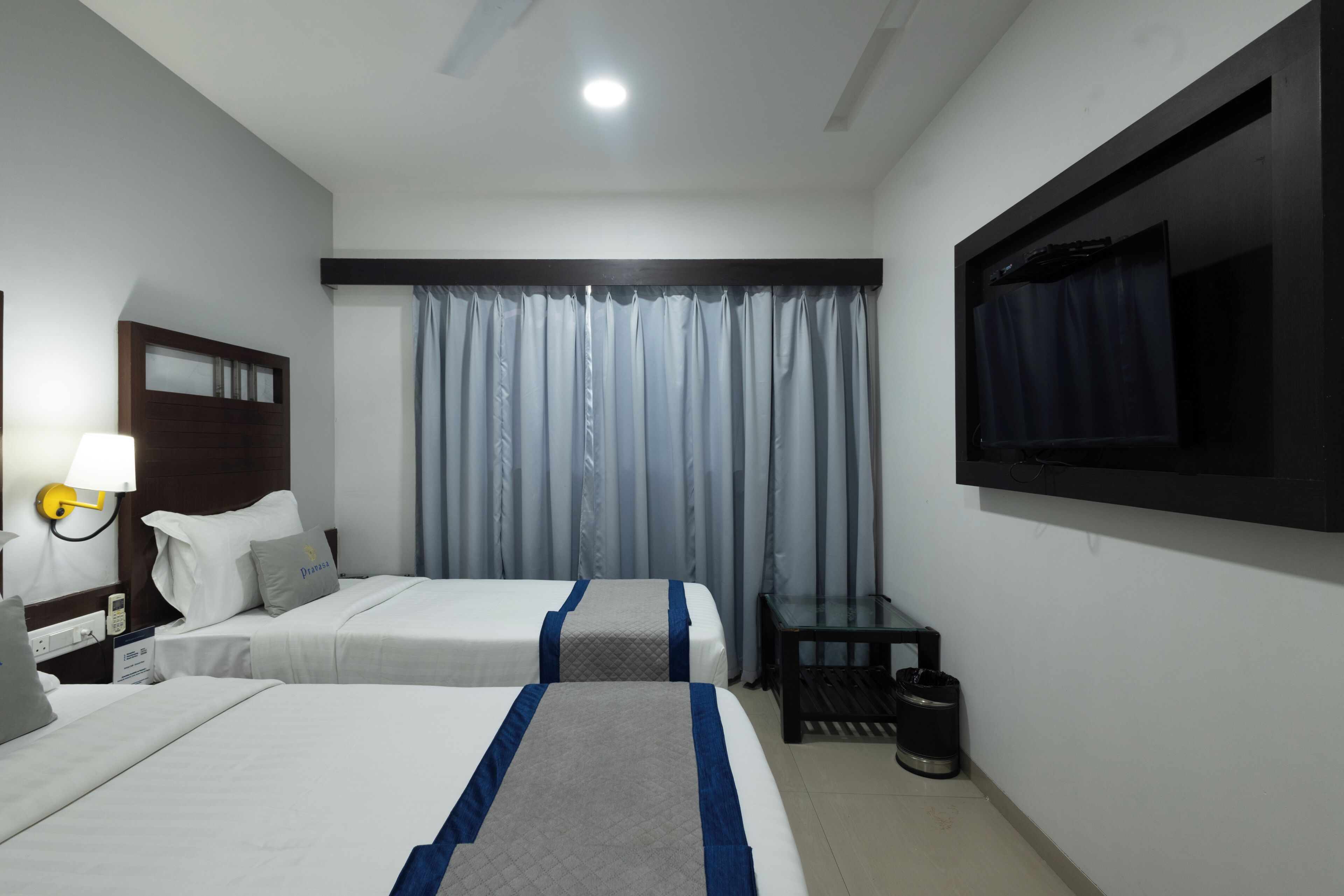 Habitación de hotel con dos camas, televisión, escritorio y ventana con cortinas.