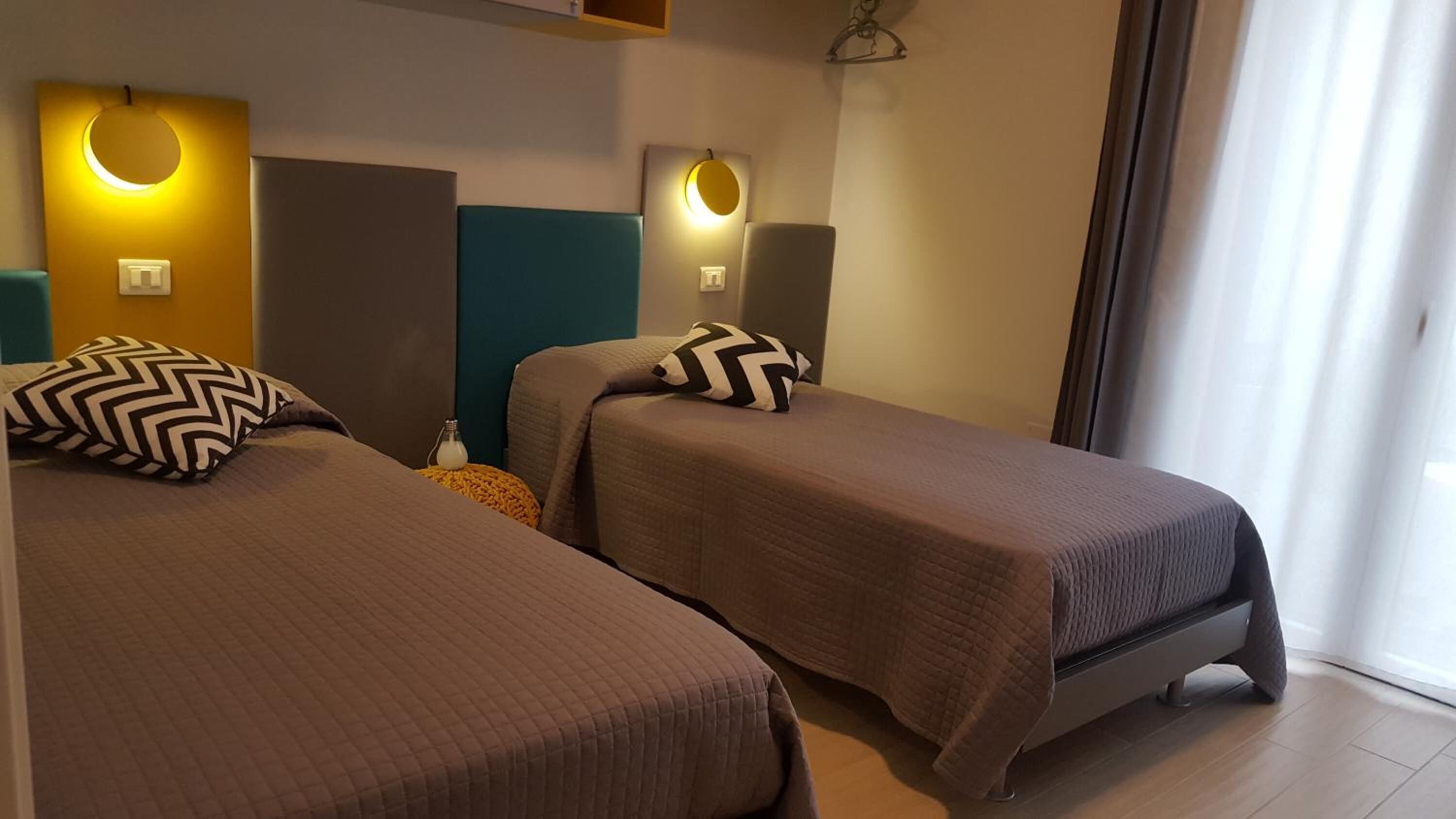Une chambre d’hôtel avec deux lits simples, chacun doté d’une tête de lit et d’un oreiller. Des appliques murales sont fixées au-dessus de chaque lit.
