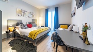 Ett modernt hotellrum med en säng, ett nattduksbord, en lampa och ett skrivbord med en stol.