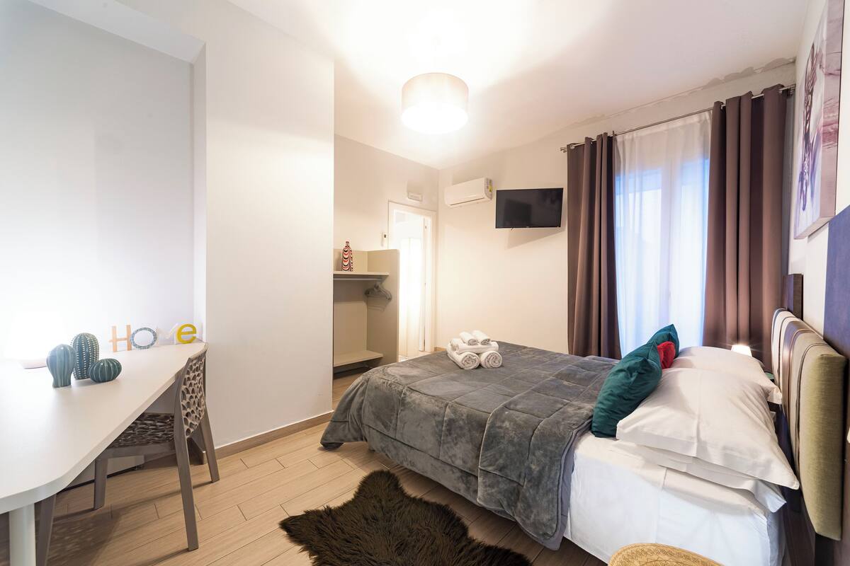 Une chambre à coucher avec un lit, un bureau, une chaise, un téléviseur et une fenêtre avec des rideaux.