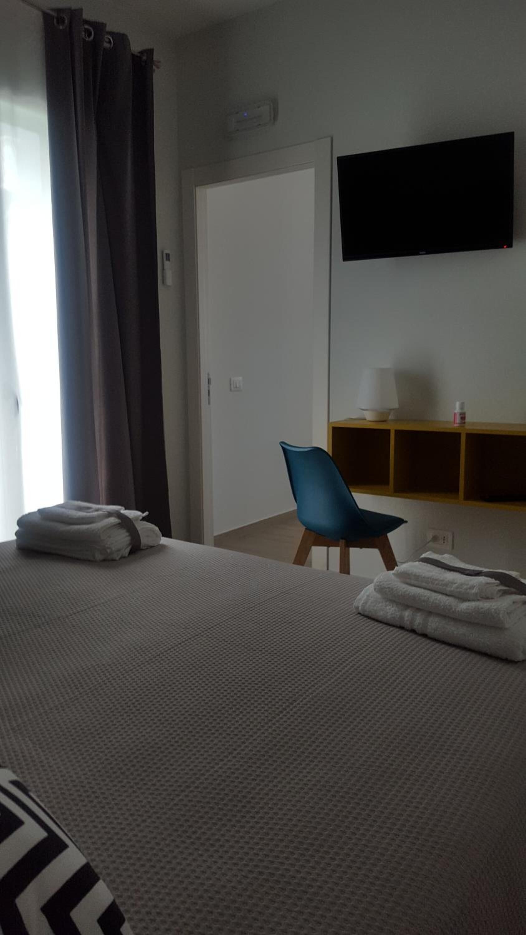 A hotel room with a bed, a chair, a TV mounted on the wall, and a door.