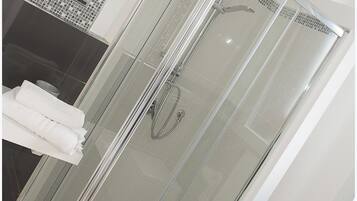 Un baño moderno con ducha de vidrio, lavamanos blanco y un perchero para toallas.
