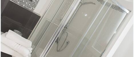 Un baño moderno con ducha de vidrio, lavamanos blanco y un perchero para toallas.