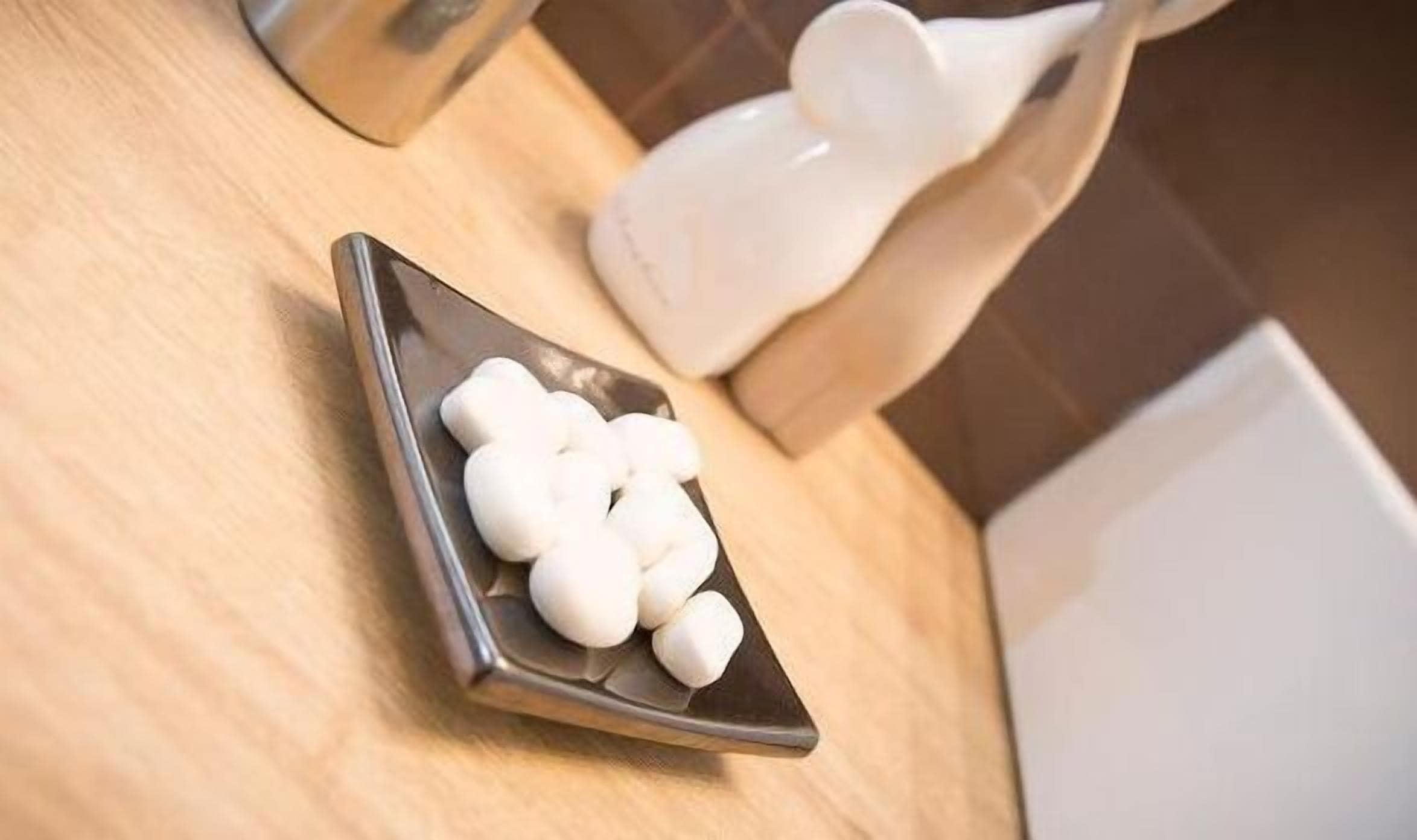 Una bandeja con sales de baño blancas sobre una encimera de madera.