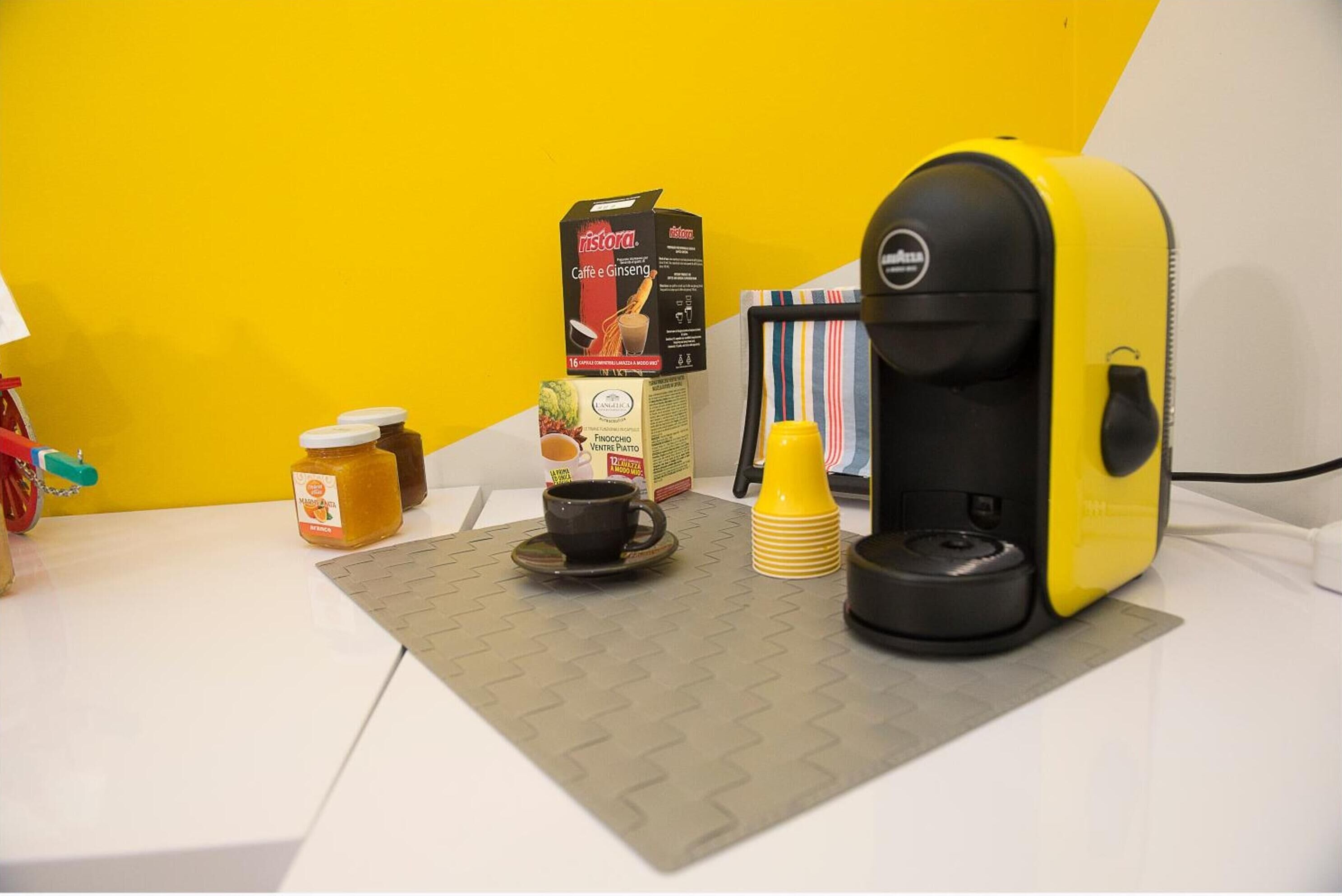 Een koffiezetapparaat, een koffiekop, een pot honing, een pak melk en een doos biscotti op een tafel.