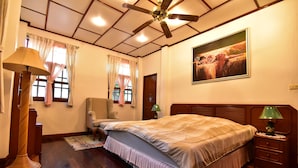 A bedroom with a bed, a ceiling fan, a nightstand, a lamp, a chair, and a painting on the wall. - Nong Apartment Pattaya - Adults Only (Pattaya)