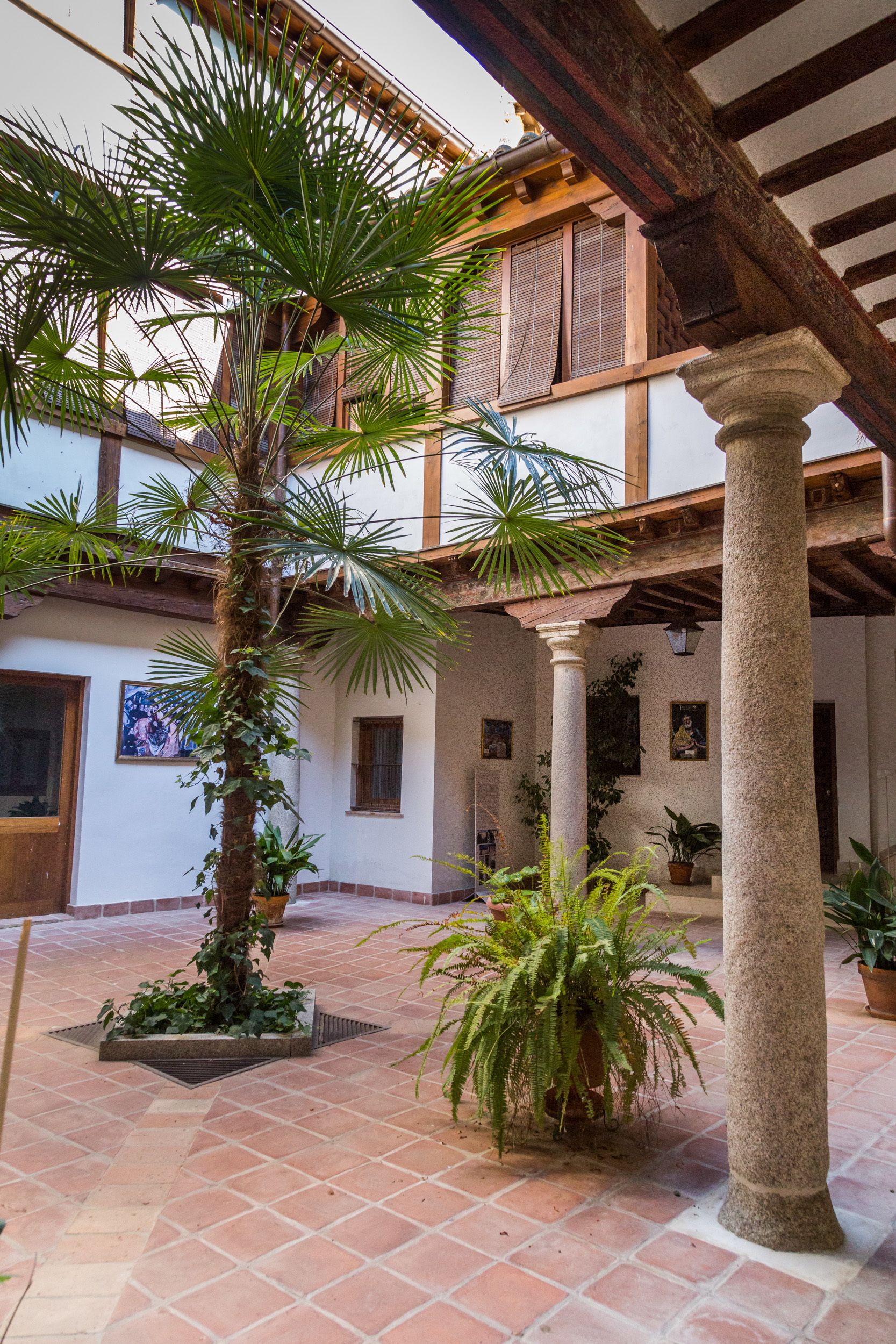 Un patio con piso de baldosas, palmeras y un edificio con vigas y columnas de madera.