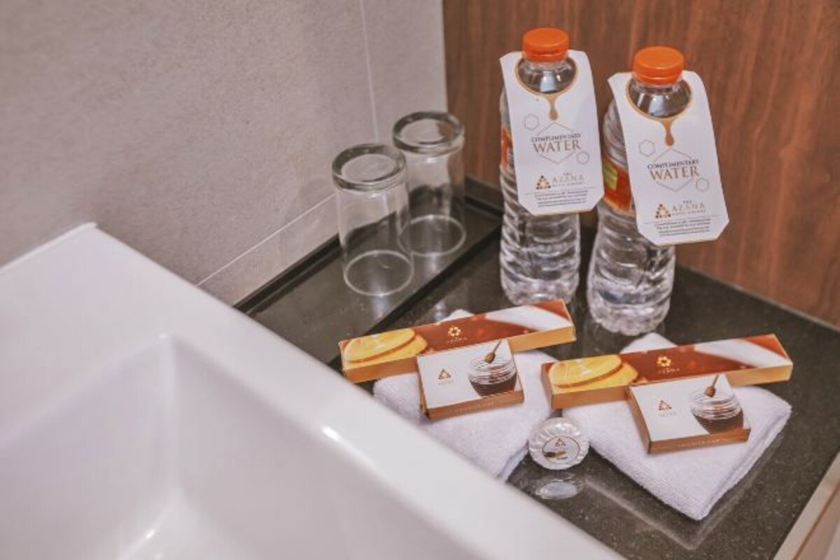 Una encimera de baño con dos botellas de agua, tres recipientes de vidrio y varios botes de artículos de aseo.