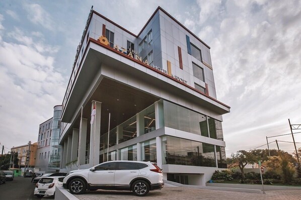 A modern hotel with a unique cantilevered structure, large glass windows, and a white car parked in front. - The Azana Hotel Airport Semarang (Semarang)