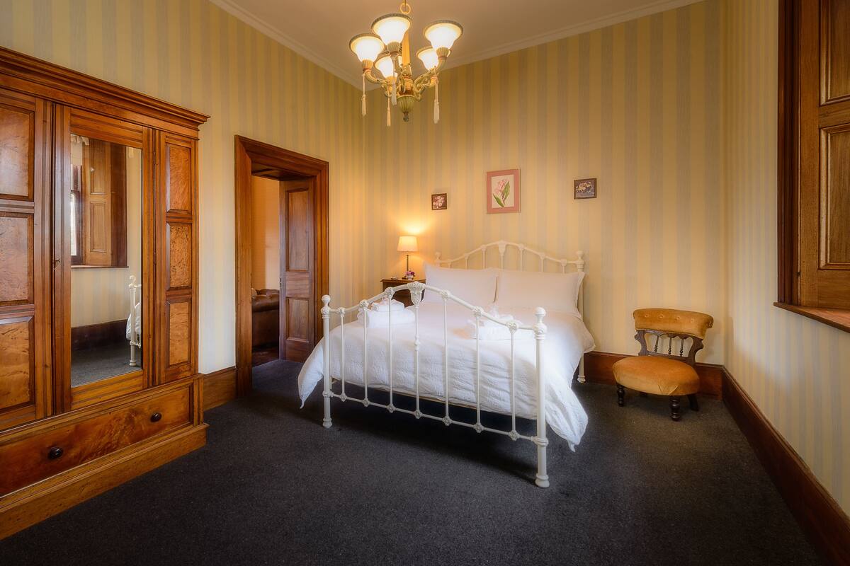 Un dormitorio con una cama de metal blanco, un armario de madera y una araña.