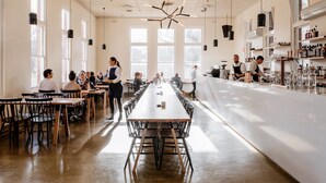 Un restaurant spacieux avec de longues tables communes, un bar et de grandes fenêtres qui laissent entrer la lumière naturelle.