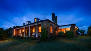 Une grande maison en pierre à deux étages, dotée d’un porche abrité et de plusieurs cheminées.