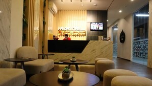 A hotel lobby with a reception desk, seating area, and a television screen. - Front One Inn Kediri (Ngasem)