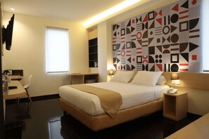 A hotel room with a bed, bedside tables, a desk, and a window.