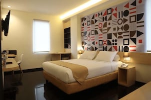 Una habitación de hotel con cama, mesitas de noche, un escritorio y una ventana.