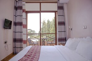 Une chambre d’hôtel avec un lit, un téléviseur fixé au mur, un balcon avec des chaises et des rideaux.