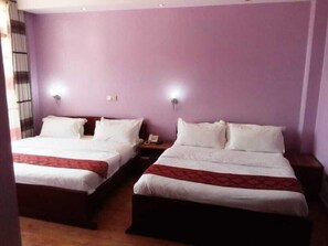 Une chambre d’hôtel avec deux lits, chacun recouvert de draps blancs et d’une couverture rouge. Il y a deux tables de chevet avec des lampes et un téléphone. Les murs sont violets et il y a une fenêtre avec des rideaux.