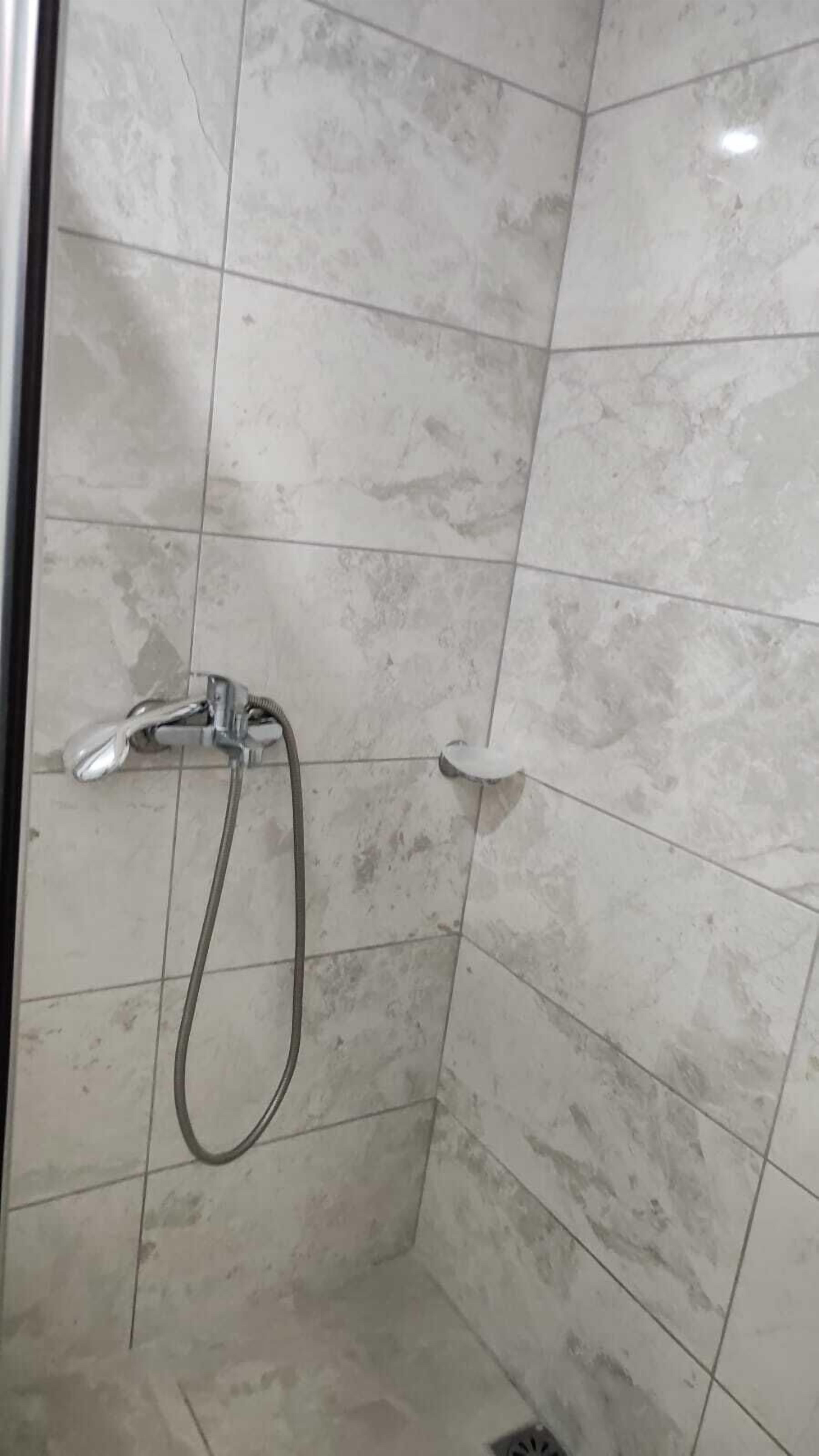 Un área de ducha con cabezal de ducha manual y grifo empotrado en la pared.