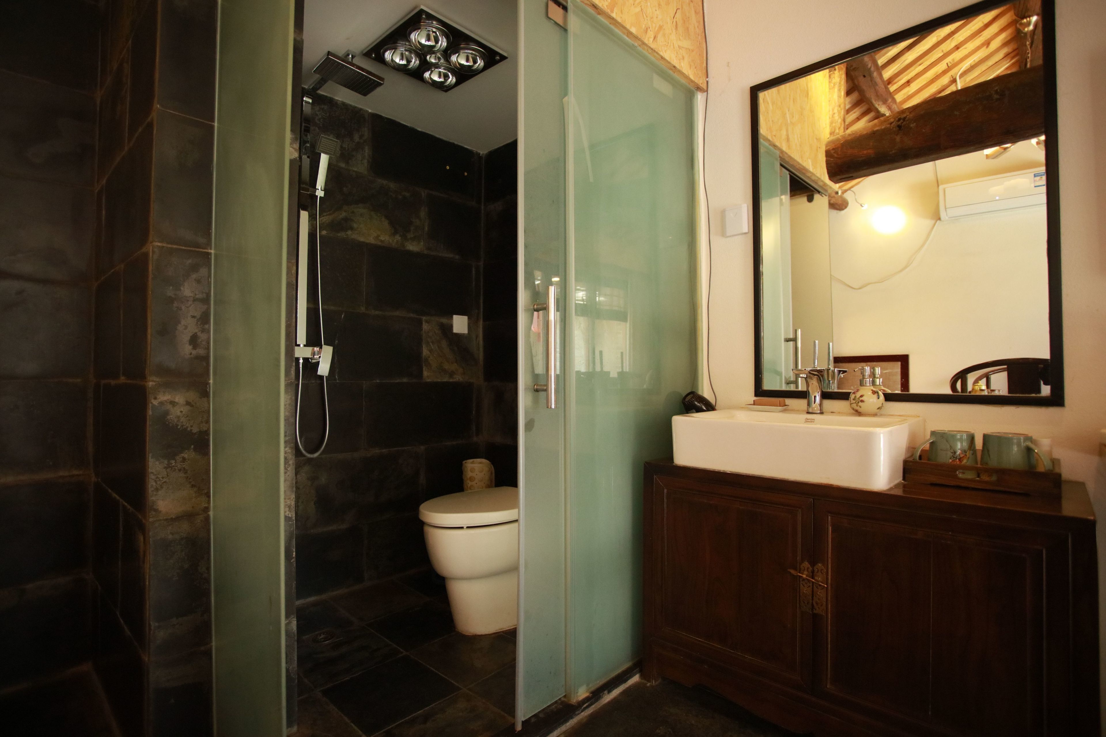 A bathroom with a glass-enclosed shower, a white toilet, a wooden vanity with a mirror, and a white sink.