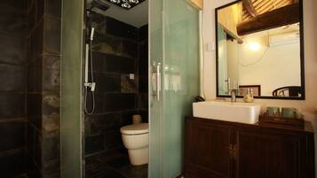 A bathroom with a glass-enclosed shower, a white toilet, a wooden vanity with a mirror, and a white sink.
