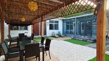 An outdoor patio with a wooden pergola, a glass table, and chairs.