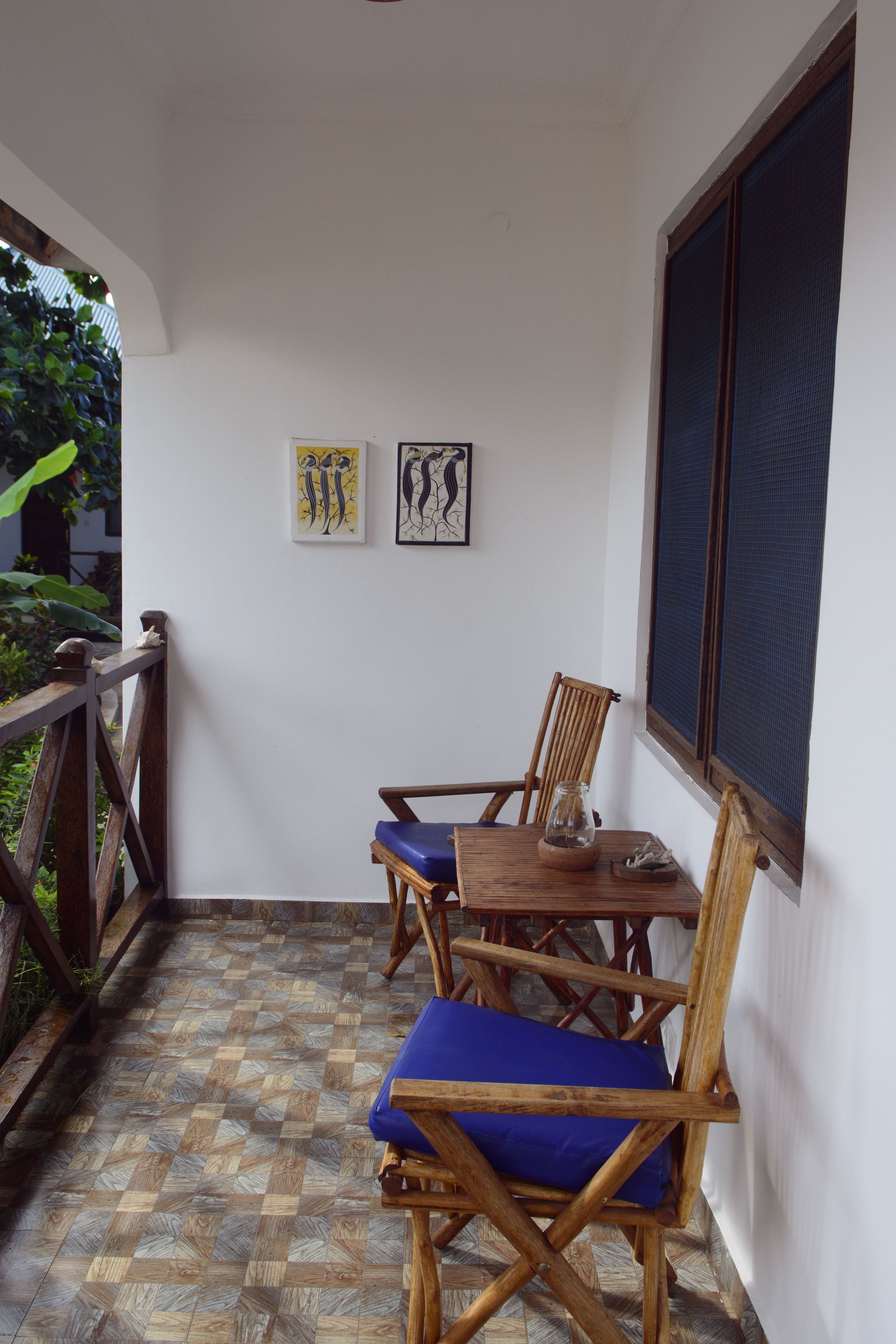 Une terrasse couverte avec une table et des chaises en bois, un petit vase et deux œuvres d’art encadrées accrochées au mur.