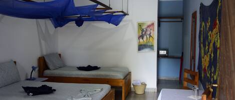 Une pièce avec deux lits en bois, un ventilateur de plafond, une table recouverte d’une nappe et un mur orné d’un tableau.