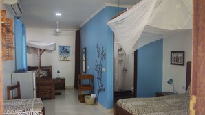 A bedroom with a bed, a desk, a chair, a small table, and a nightstand. - Highland Bungalows (Nungwi)