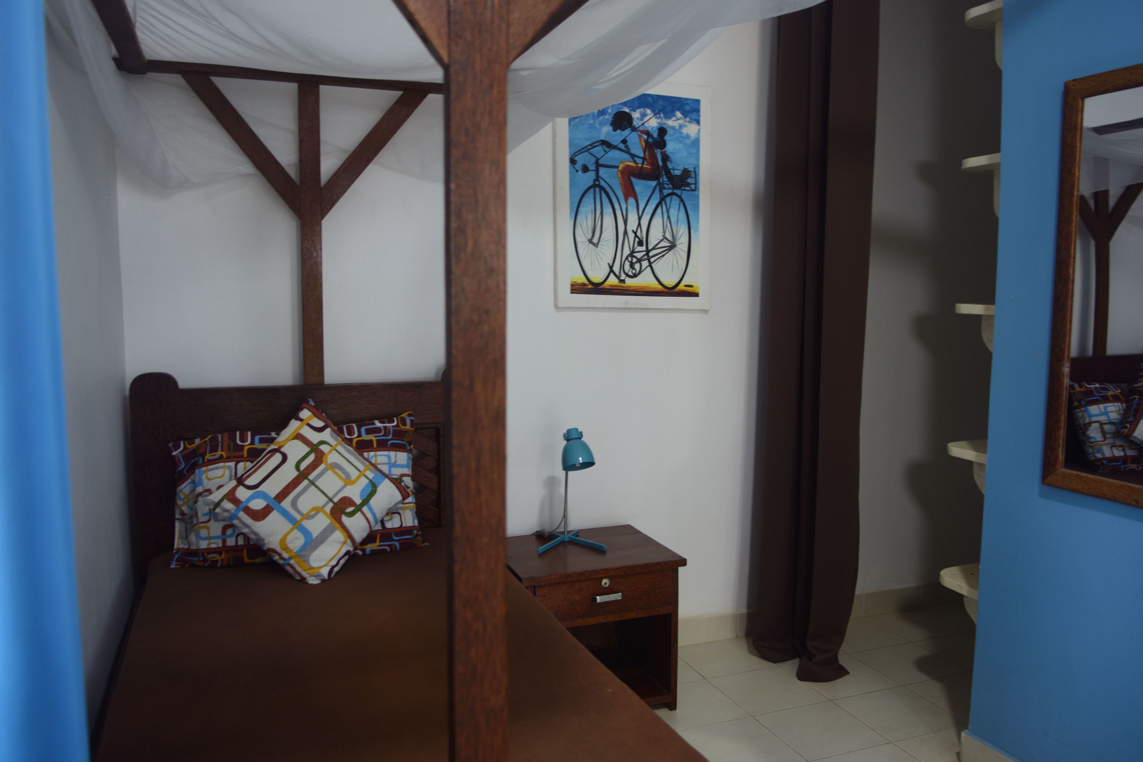 Un dormitorio con cama de madera, una mesita de noche con lámpara, un cuadro enmarcado en la pared y una pared azul.