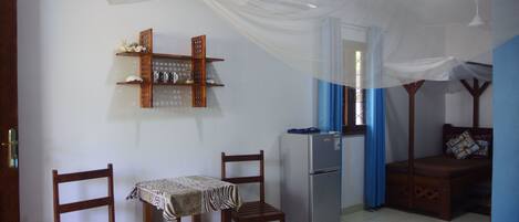 Una habitación compacta con una mesa de comedor, sillas, un refrigerador, una cama con dosel y un estante con adornos.