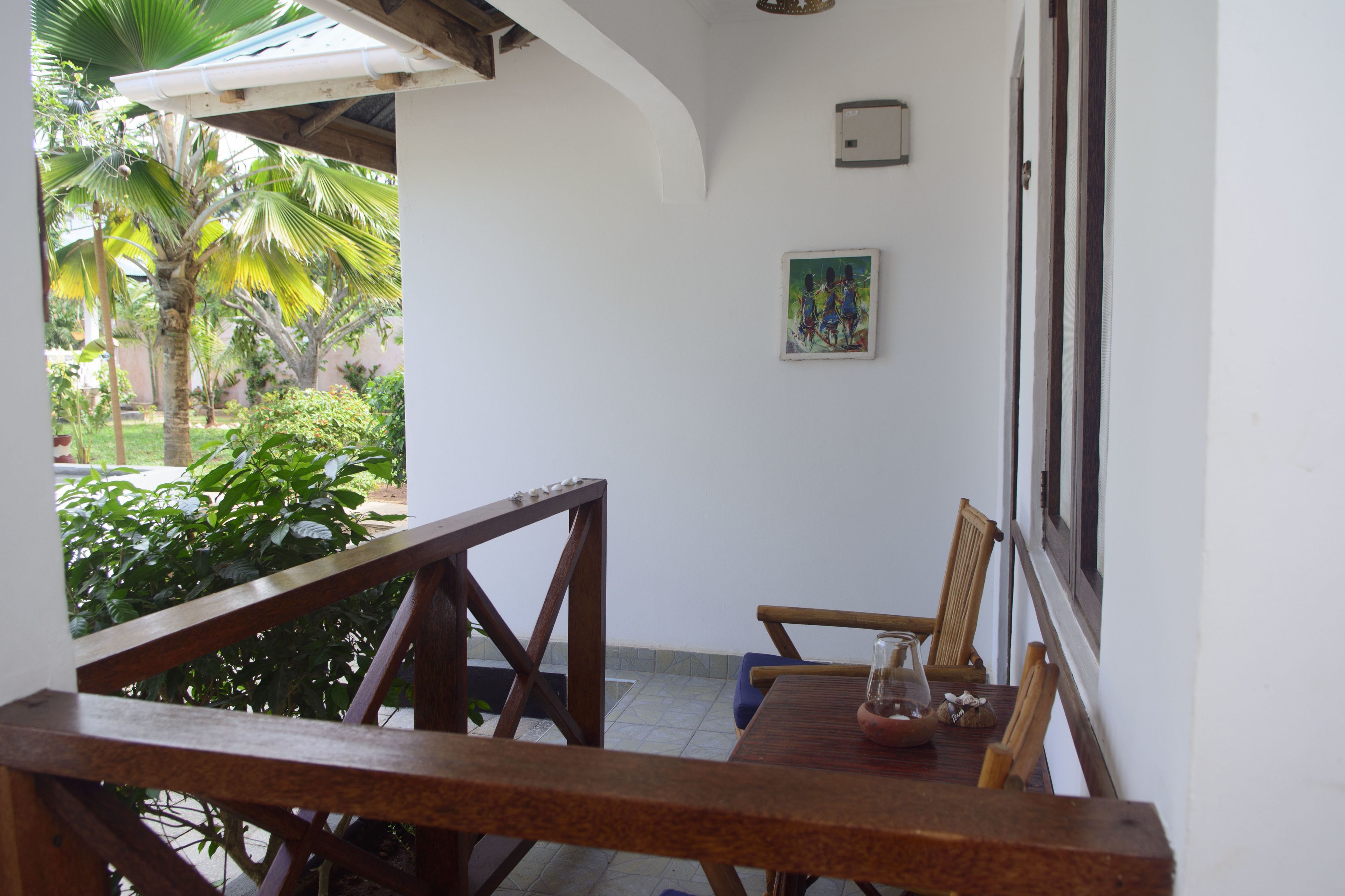 A wooden table with chairs, a painting on the wall, and a view of a garden with palm trees.