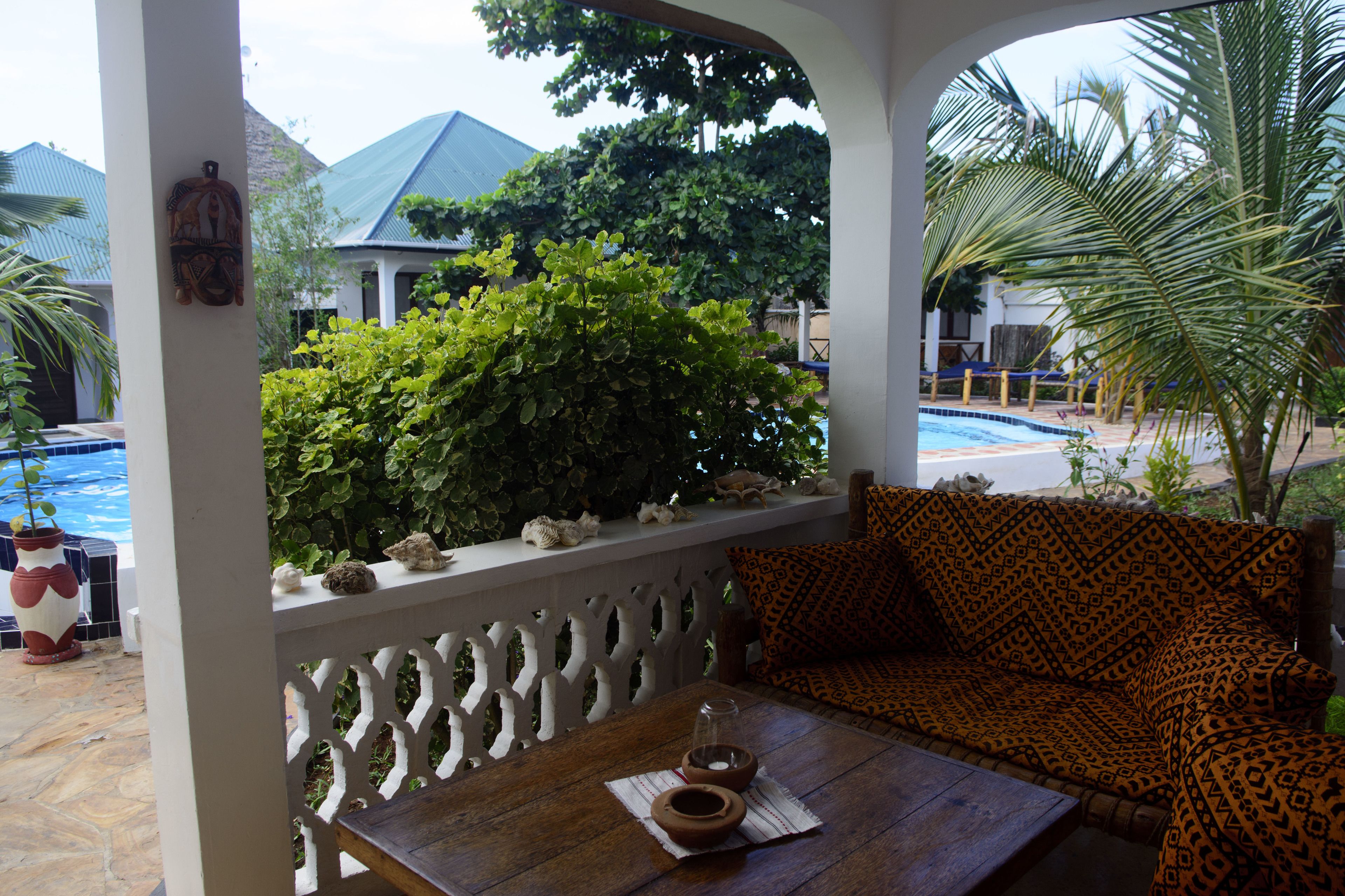 A covered outdoor seating area with a pool view, a wooden table with a bowl, and a patterned sofa.