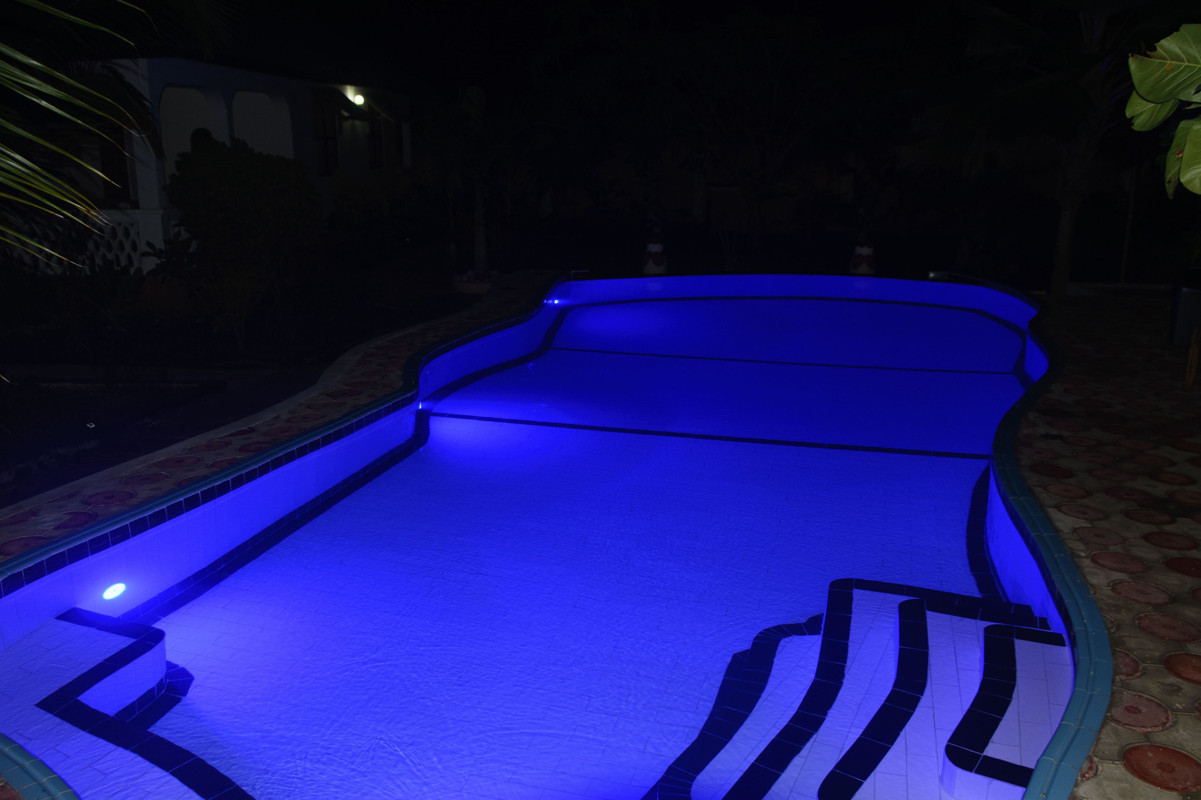 A swimming pool with blue lighting, surrounded by a tiled deck.