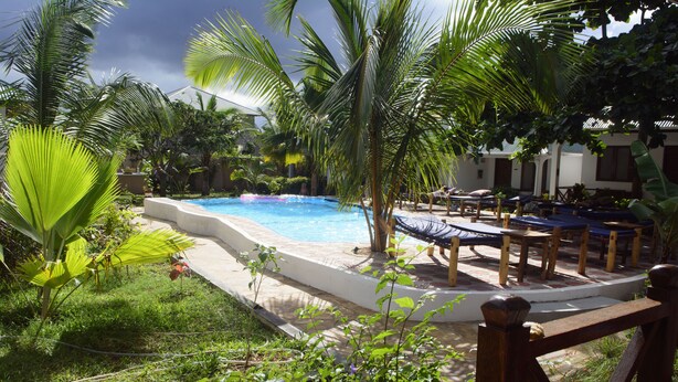 A pool area with lounge chairs and a small waterfall feature. - Highland Bungalows (Nungwi)