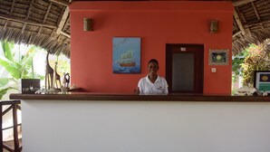 A reception desk with a red wall, a painting of a sailboat, and a wooden door. - Highland Bungalows (Nungwi)
