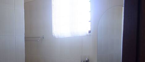 Ein Badezimmer mit weißen Fliesen, einem Fenster mit Vorhang, einem Waschbecken und einem Spiegel.