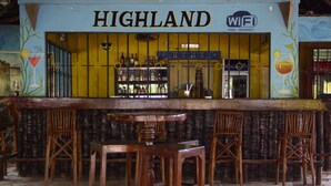 A bar area with a sign reading "HIGHLAND" and a WiFi symbol. There are wooden stools and a bar counter. - Highland Bungalows (Nungwi)