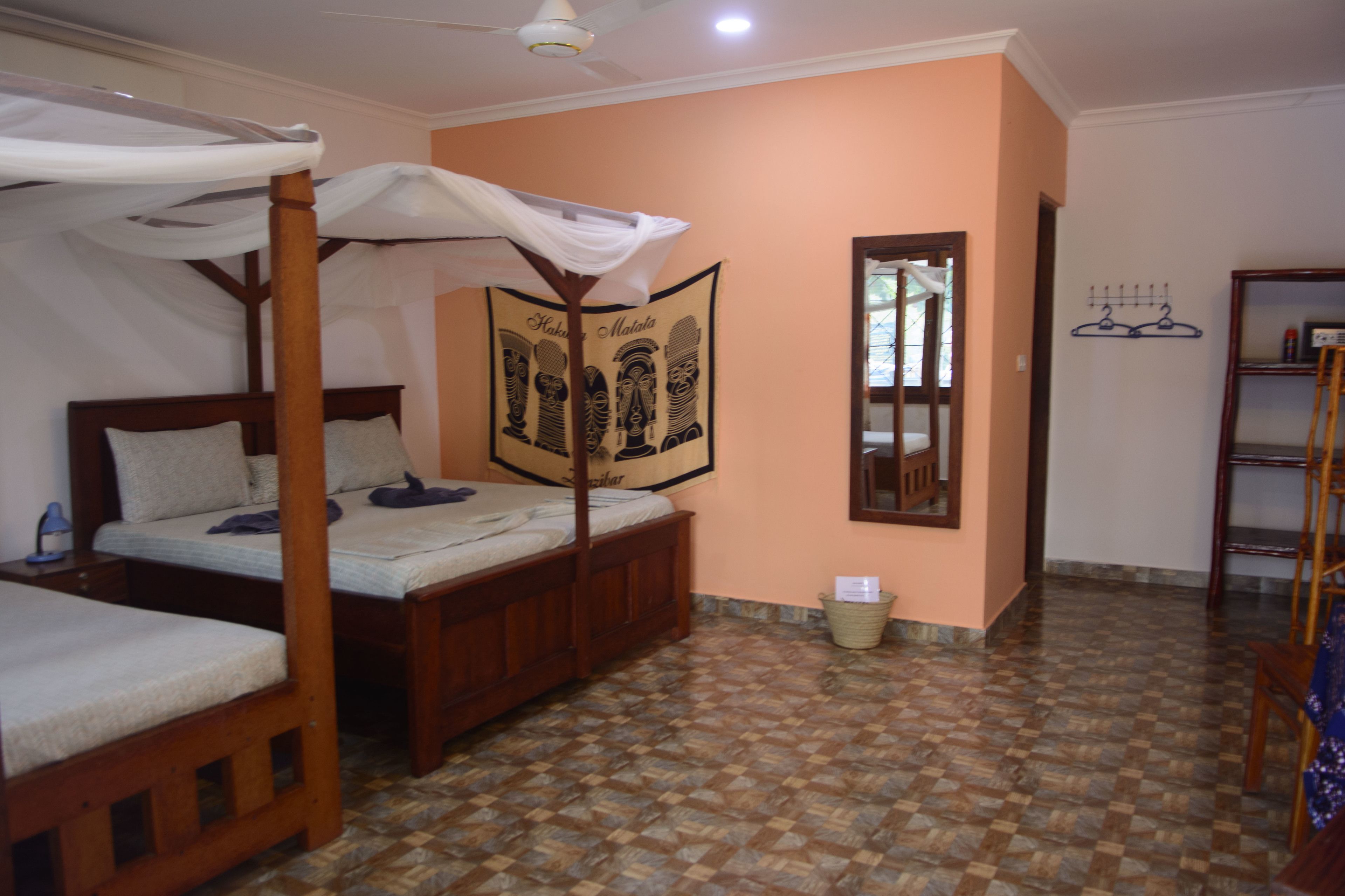 A bedroom with two wooden beds, a mosquito net, a wall tapestry, a mirror, and a shelf with hangers.