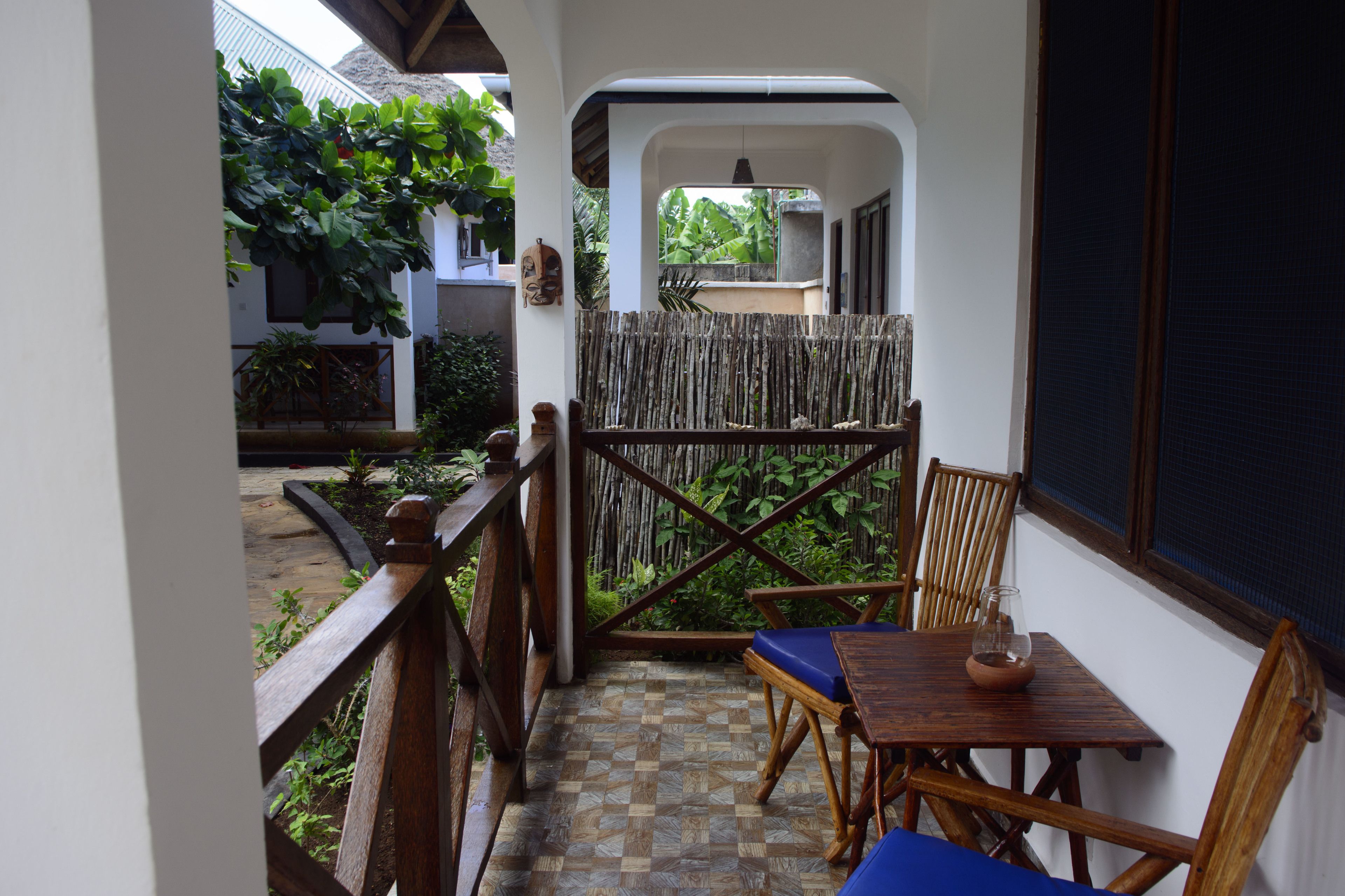 A balcony with a wooden table, chairs, and a view of a garden.