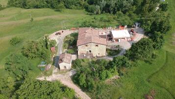 An aerial view of a rural property with a stone house, a fenced yard, and surrounding greenery.
