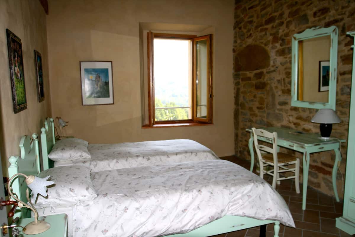 A bedroom with two beds, a desk, a chair, a mirror, and a window with a view.
