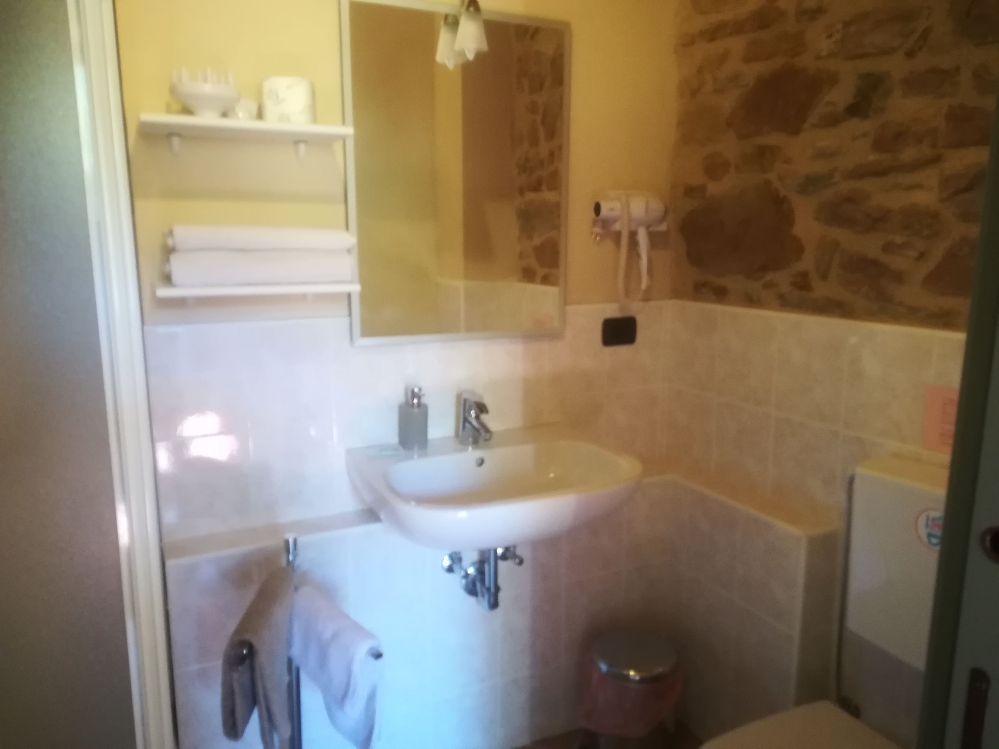 A bathroom with a white sink, mirror, and towel rack. There is a stone wall and a toilet visible.