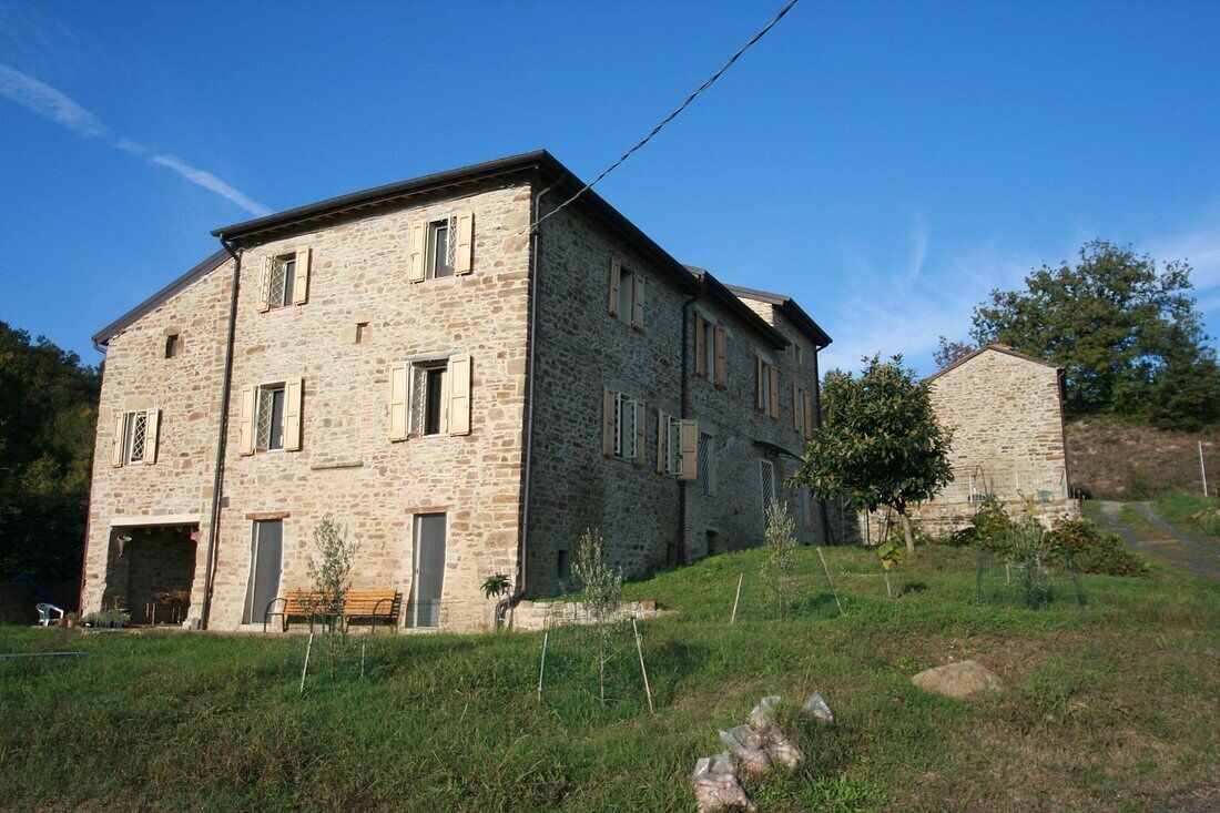 A stone building with multiple windows and a door, surrounded by grass and trees.