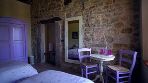 A room with a stone wall, a bed, a table with chairs, and a mirror. - Sacreterre Room & Breakfast (Tizzano Val Parma)