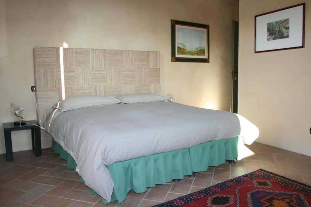 A bedroom with a bed, a nightstand, a framed picture on the wall, and a patterned rug.
